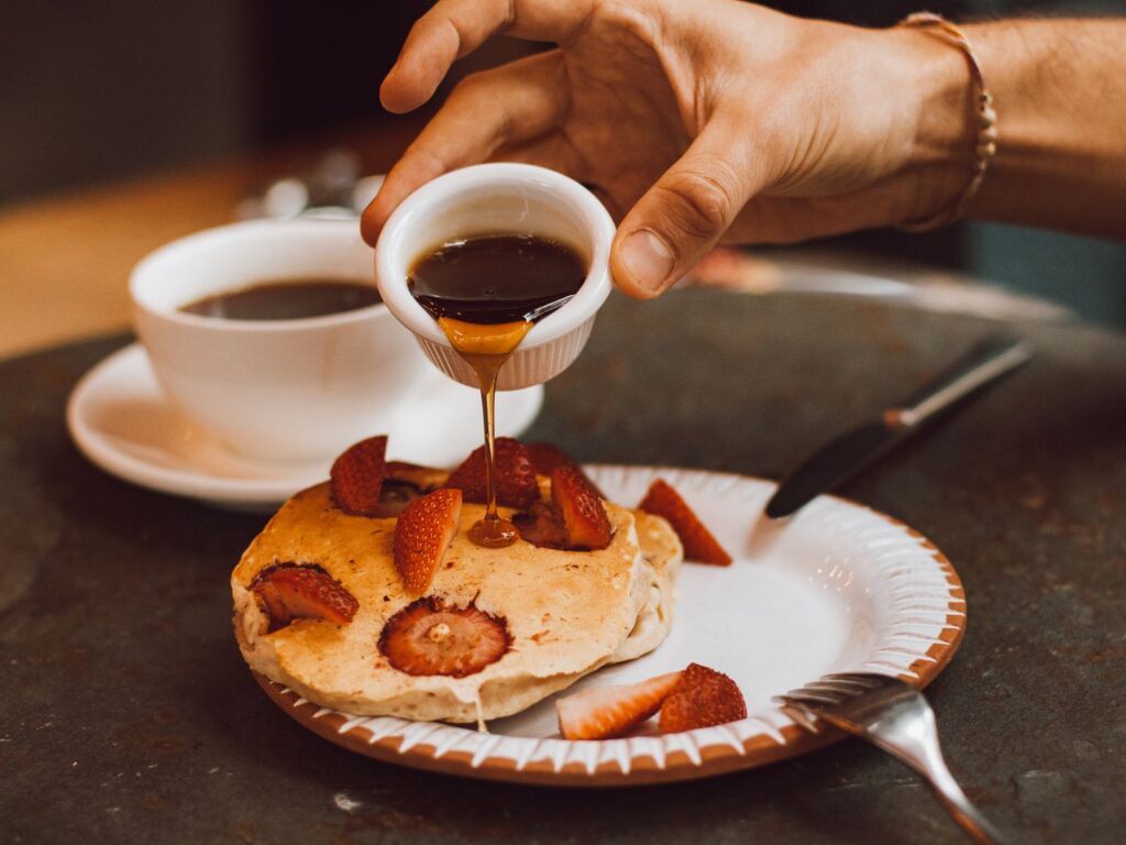 Close-up shot of pancakes topped with strawberries and maple syrup, served with coffee.