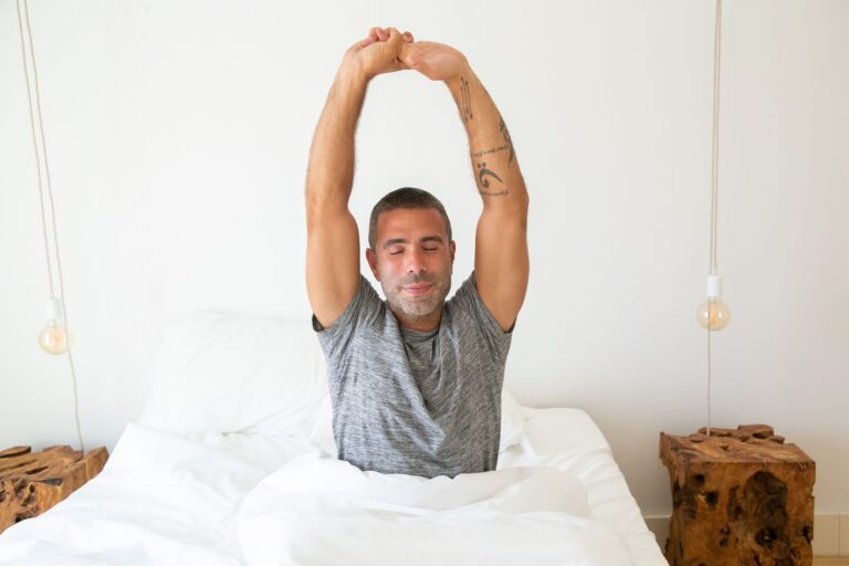 A man stretching his arms while waking up in bed, starting the morning with energy.