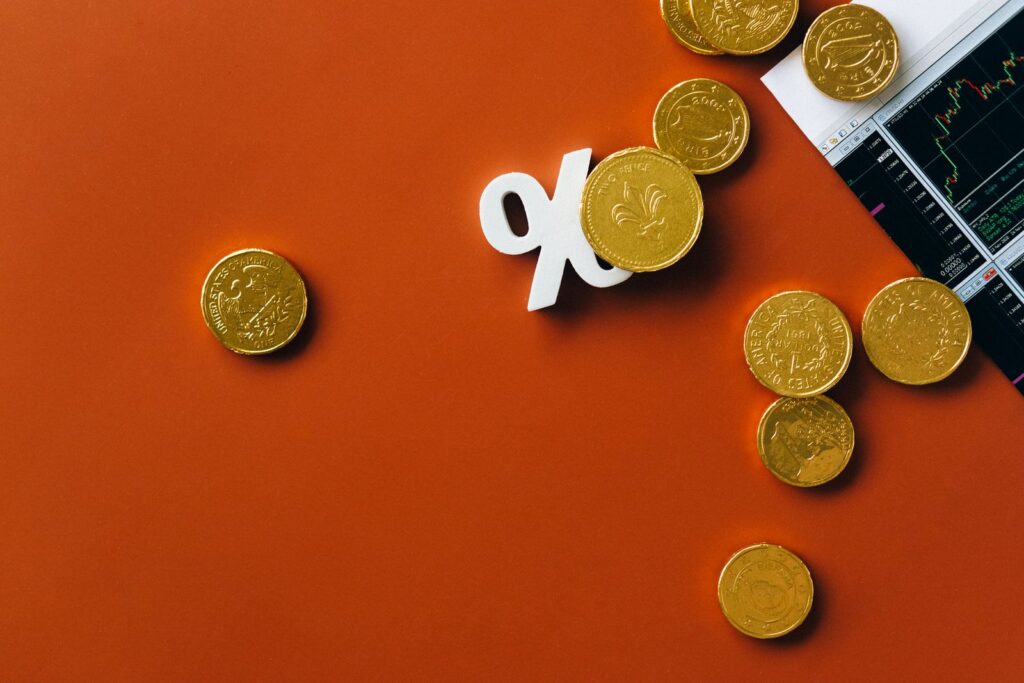 Gold coins scattered with a stock market graph and a percentage symbol on an orange background.