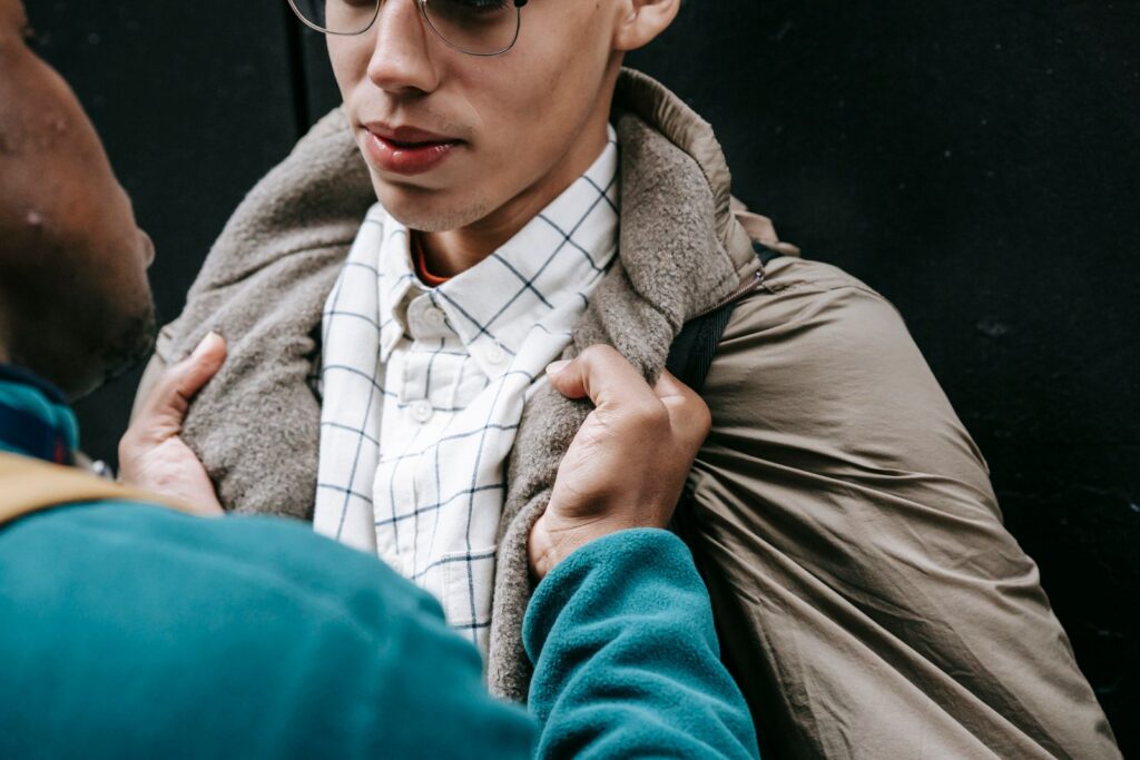 Crop faceless African American male threatening student with backpack while standing near building