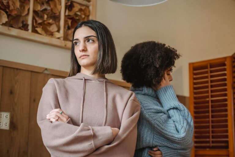 Multiracial women in casual clothes with crossed arms standing in light room during quarrel at home