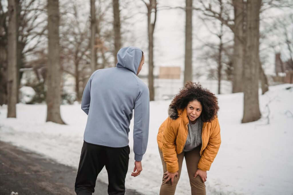 Tired African American female with excess weight having break in cardio training in winter park with coach