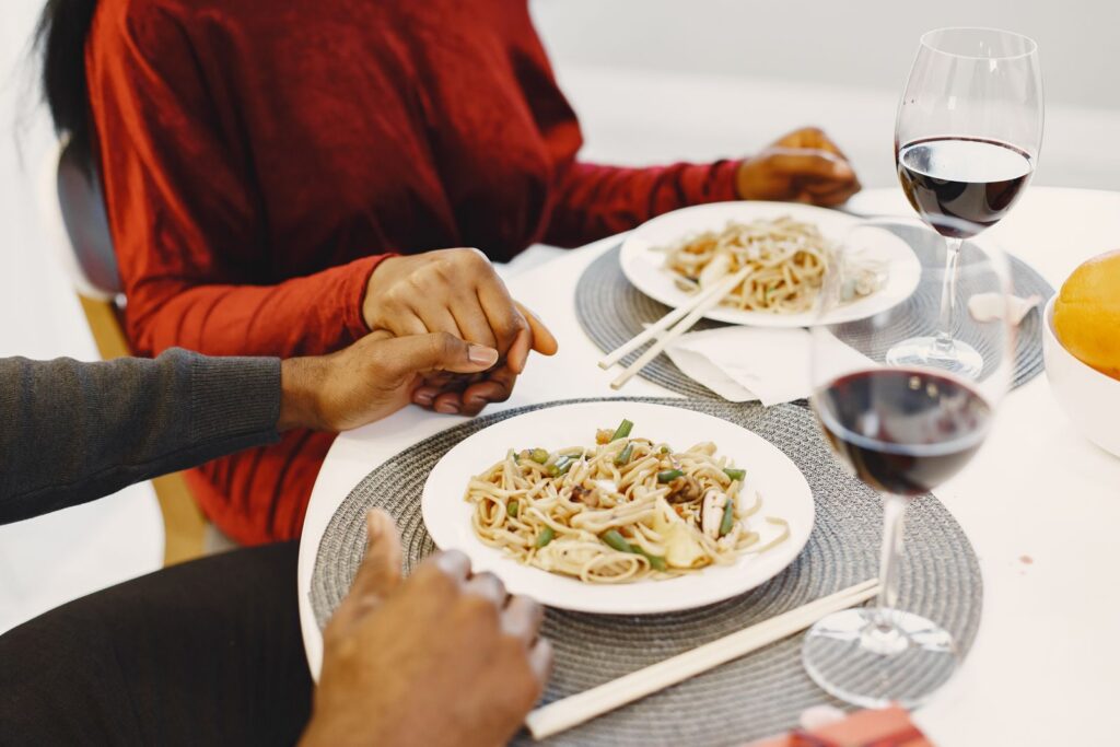 Couple enjoying a romantic dinner with red wine and pasta in a cozy restaurant setting.