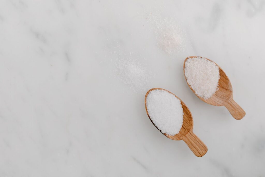 Wooden spoons filled with salt on a white marble background, top view.