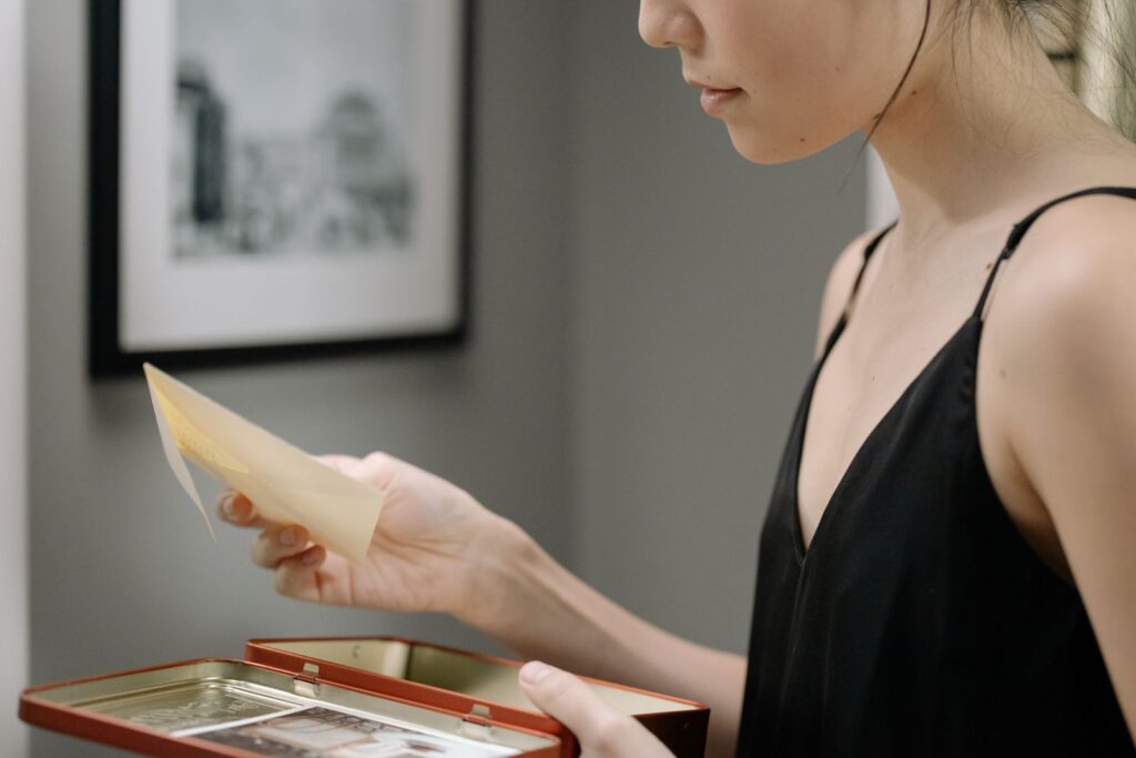 A woman in a black dress holds a photograph from an open keepsake box indoors.