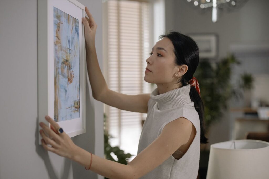 Side profile of a woman hanging framed artwork indoors. Modern decor theme.