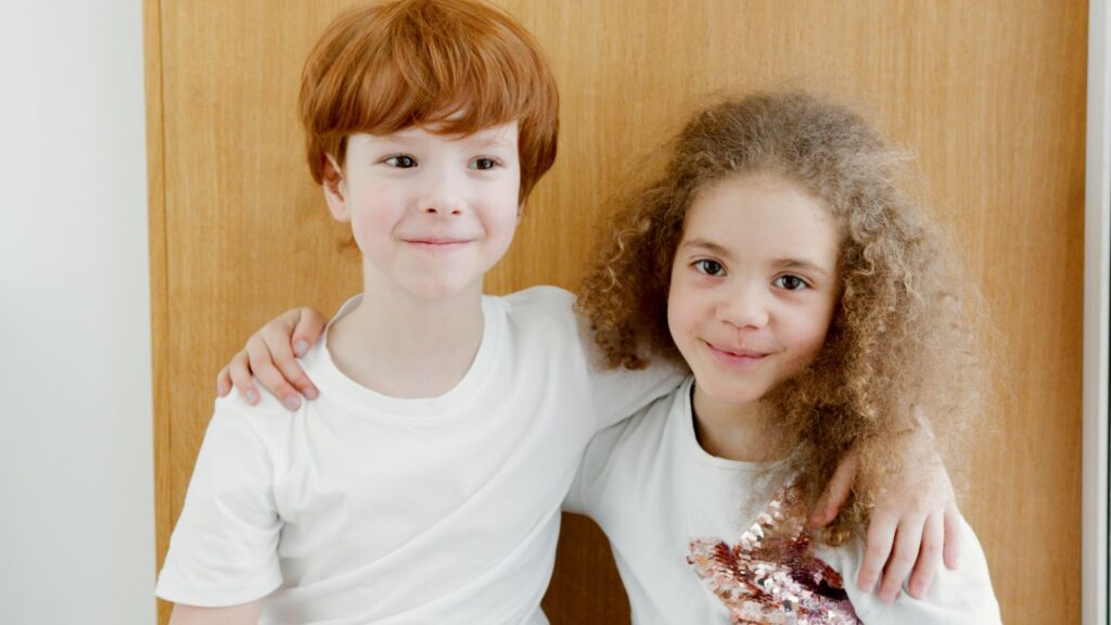 Two happy children with arms around each other indoors, showcasing friendship.