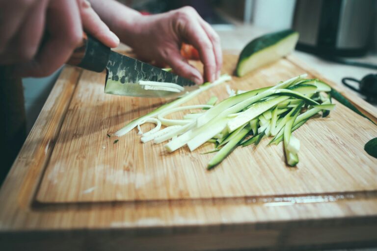 person slicing cucumber on cutting board with juice groove