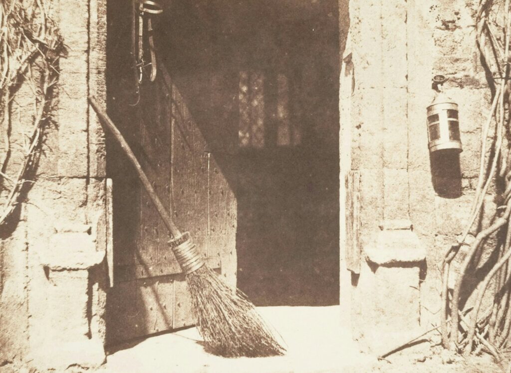 Broom leaning by an open doorway with a hanging lantern.