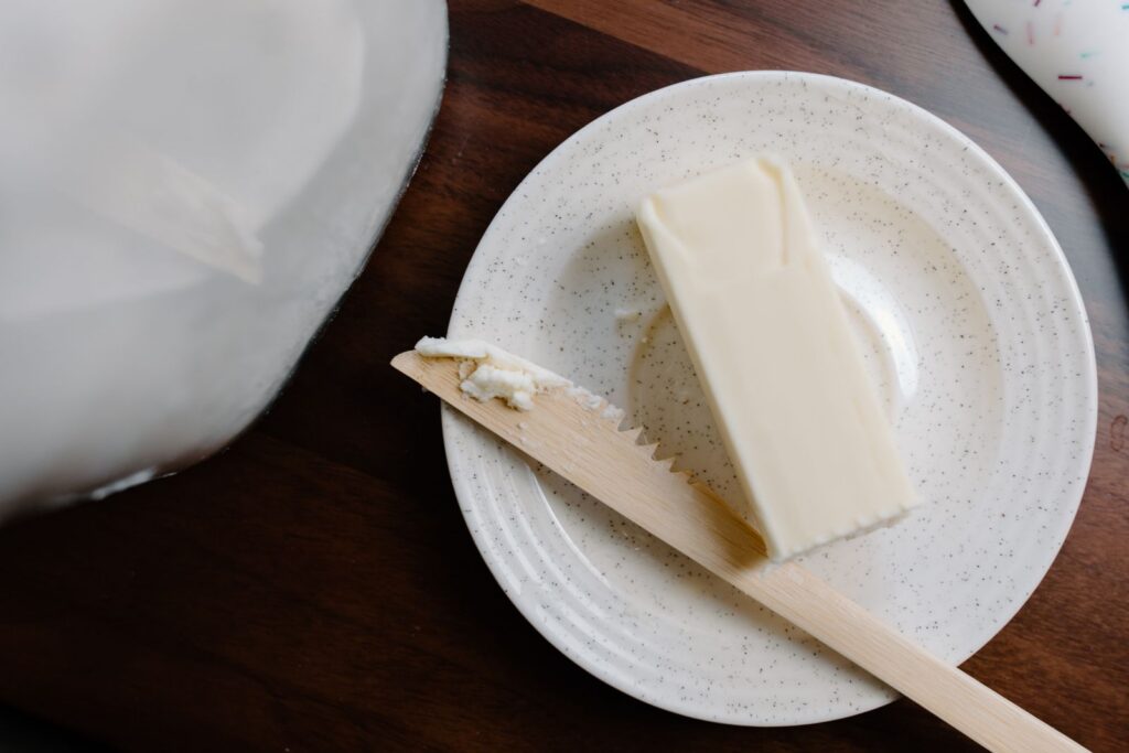 A stick of butter on a rustic plate with a wooden knife against a dark wooden surface.