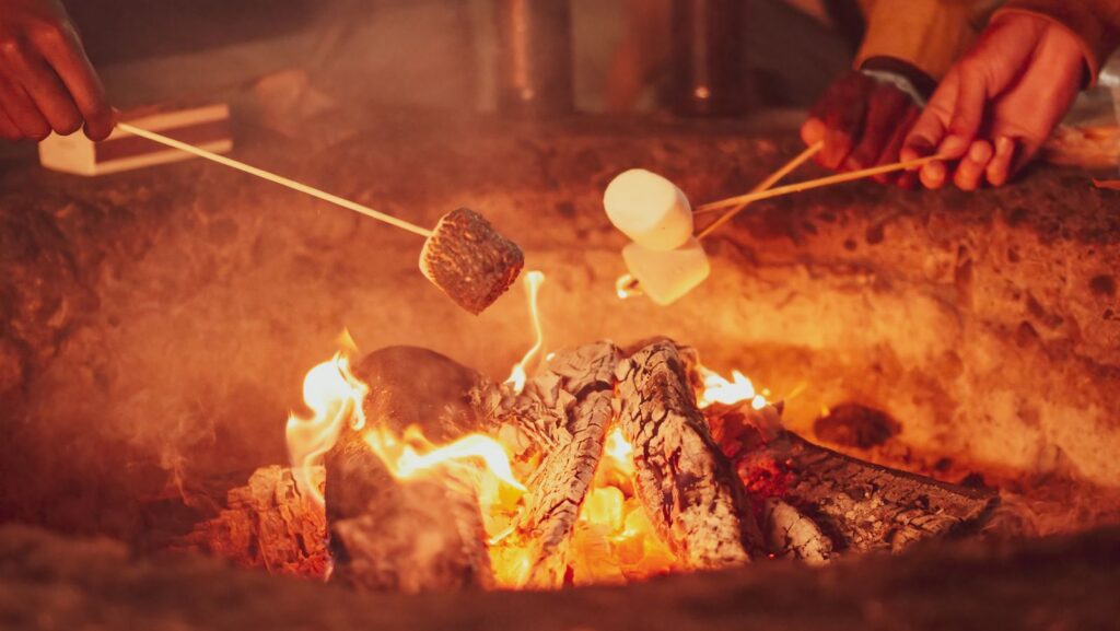 Close-up of hands roasting marshmallows over a campfire at night, creating a cozy atmosphere.