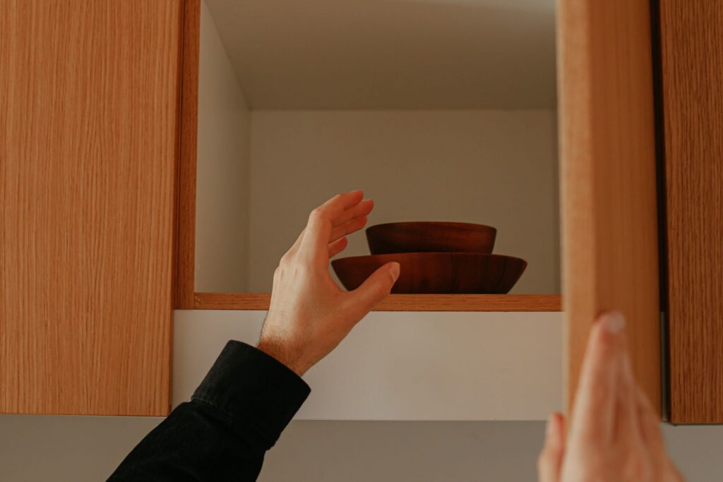 A person reaching into a wooden kitchen cabinet to retrieve stacked wooden bowls.