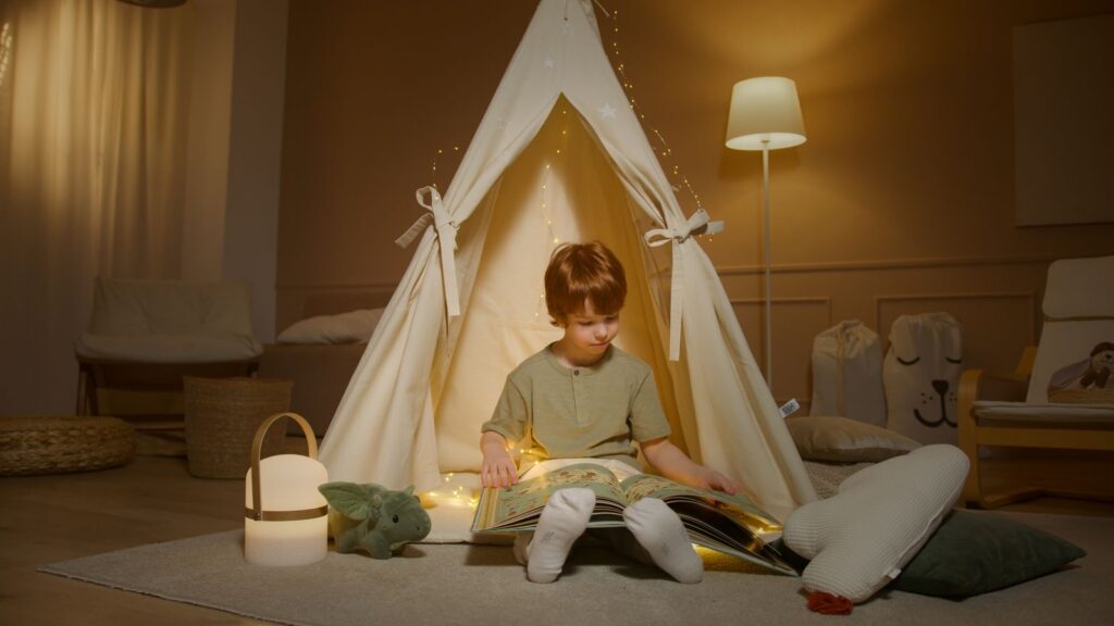 Young boy reading a book in a cozy tent with warm lighting indoors, perfect for storytelling.