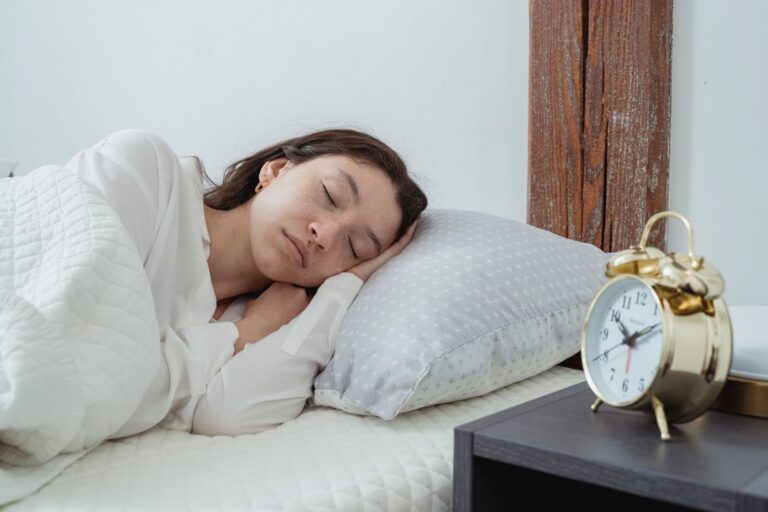 Young calm female with dark hair lying on side with hand under head on white comfortable bed under blanket while sleeping in morning time