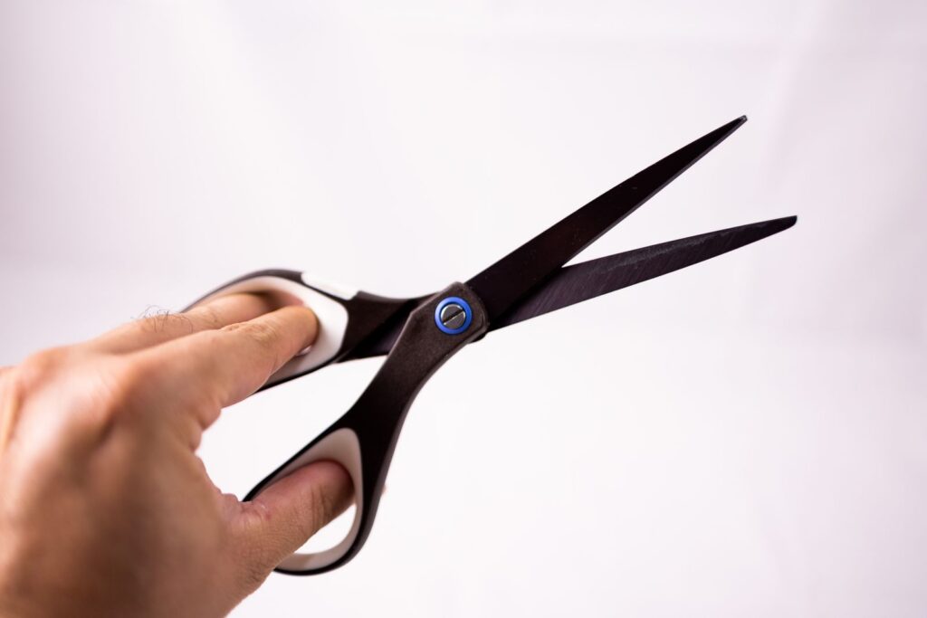 Crop anonymous person demonstrating and opening sharp scissors on white background in studio