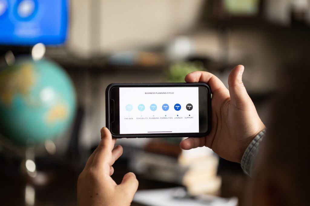 Close-up of hands holding a smartphone displaying a business planning cycle diagram.