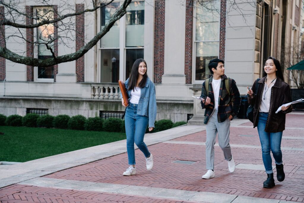 Group of young students walking on campus sidewalk on a bright day, showcasing casual university life.