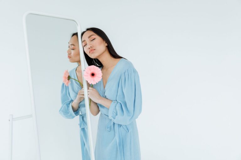 A serene portrait of a woman in a blue dress holding a pink gerbera flower, reflected in a mirror.
