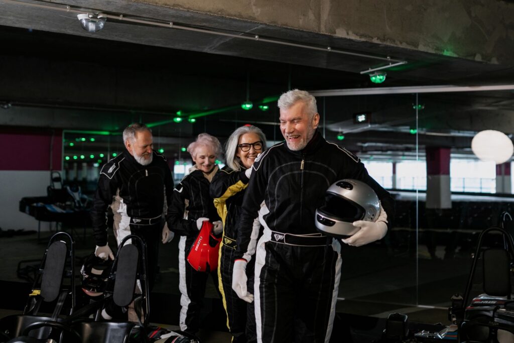 Group of senior adults having fun go-kart racing indoors with safety gear.
