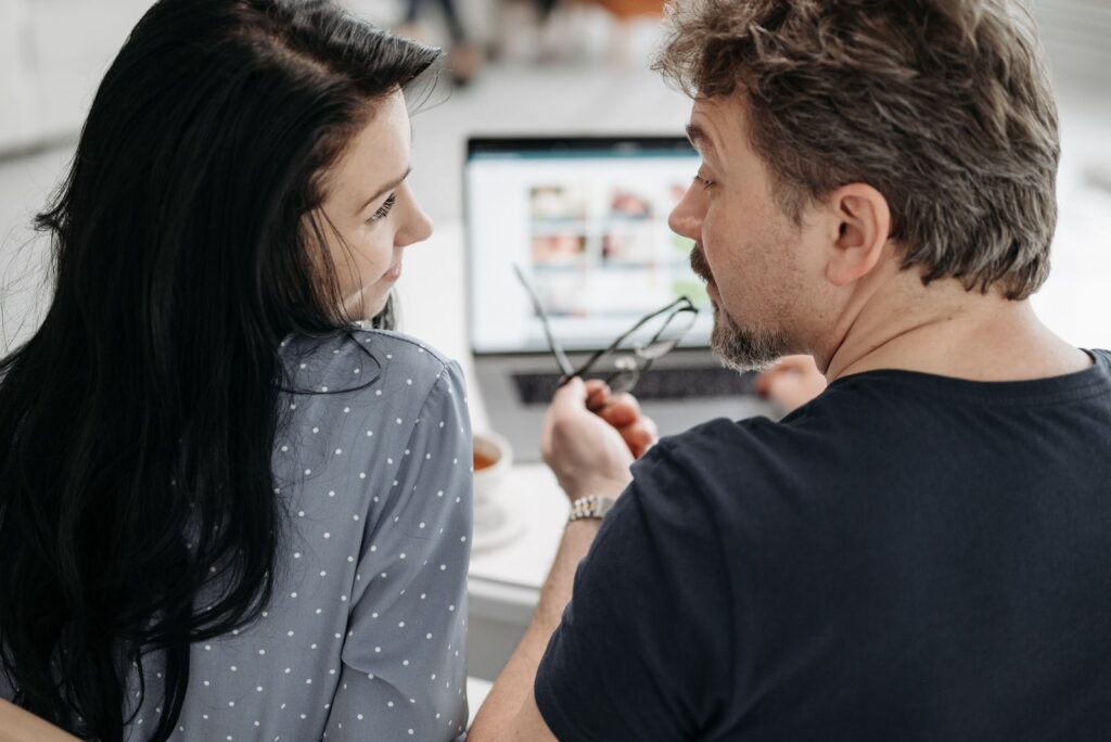 A couple having a conversation while working together on a laptop indoors.