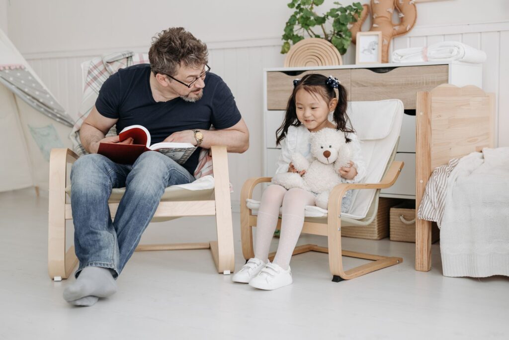 A father and daughter share a bonding moment while reading books together indoors.