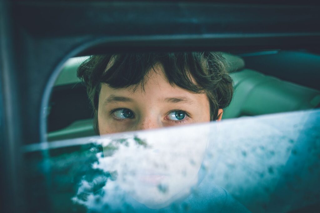 A thoughtful child with blue eyes looks through a car window, creating a reflective mood.