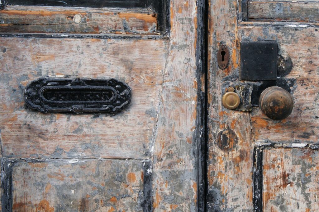 Close-up of a weathered wooden door with an old mail slot and vintage handle, showcasing rustic charm.