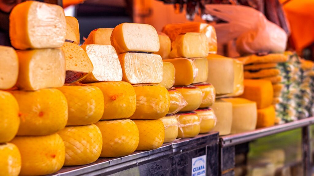 Close-up of various cheeses wrapped and displayed on a market shelf.