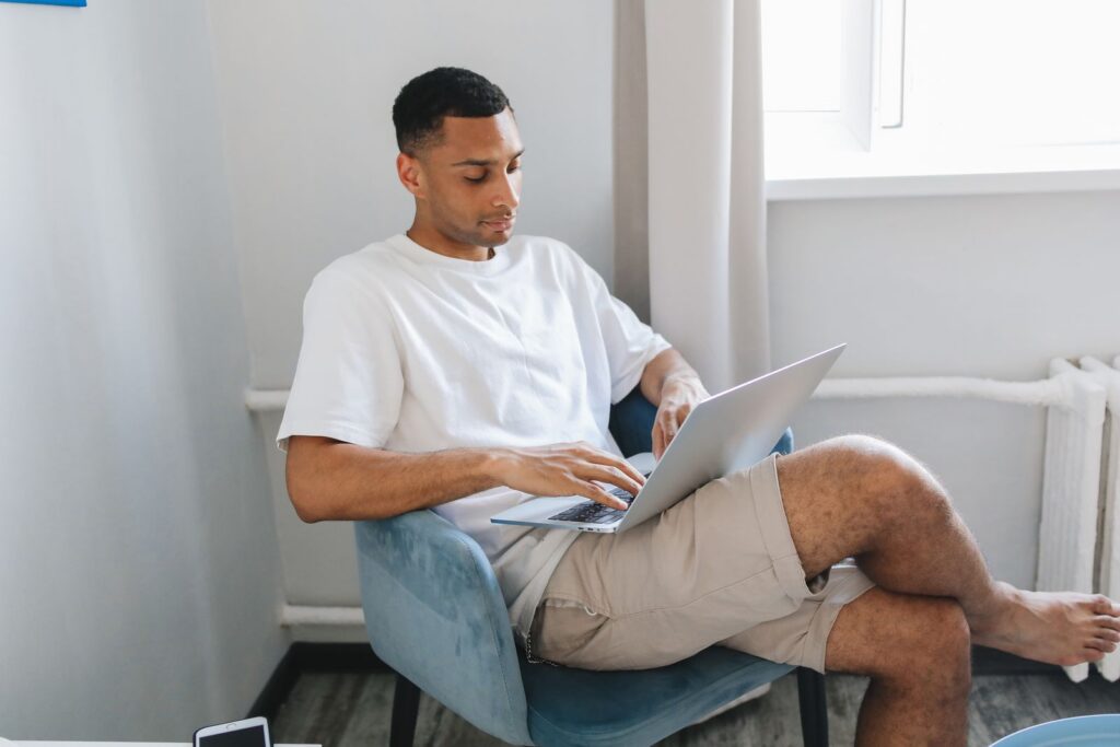Young man focused on typing on a laptop while sitting in a comfortable chair.