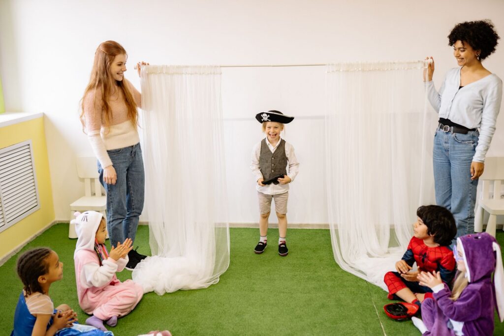 Group of kids and teachers enjoying a costume play in a preschool classroom.