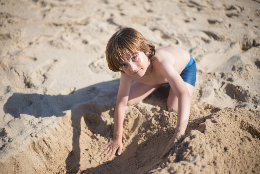 A young boy in blue shorts playing in the sand on a sunny beach day.