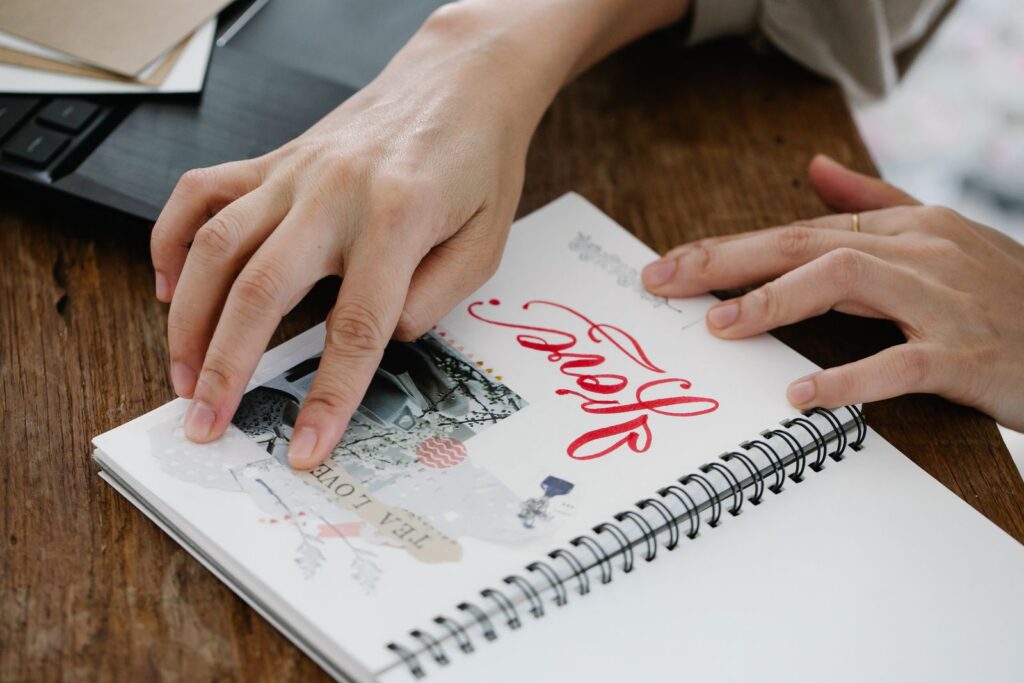 Hands crafting in a scrapbook, displaying creativity and art with Latin script text.