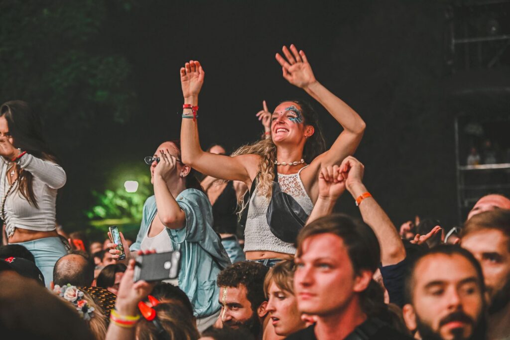 Energetic crowd enjoying a vibrant evening concert with a focus on a smiling woman dancing.