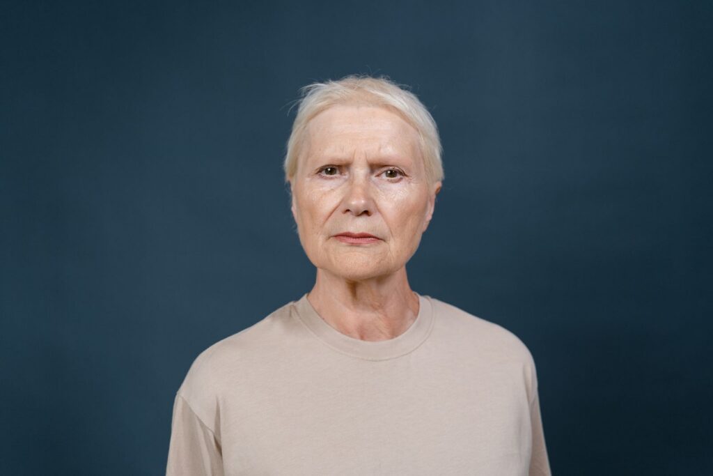 Studio portrait of a senior woman with blonde hair looking confidently at the camera against a blue background.