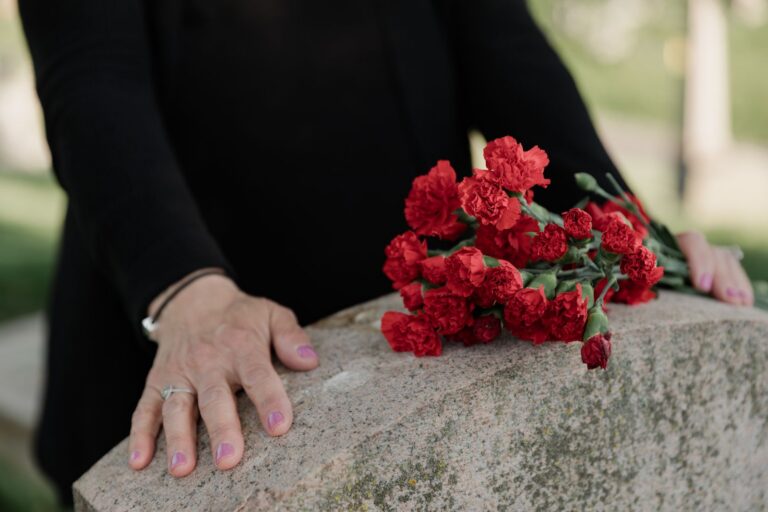 A woman dressed in black stands solemnly by a tombstone with red carnations.