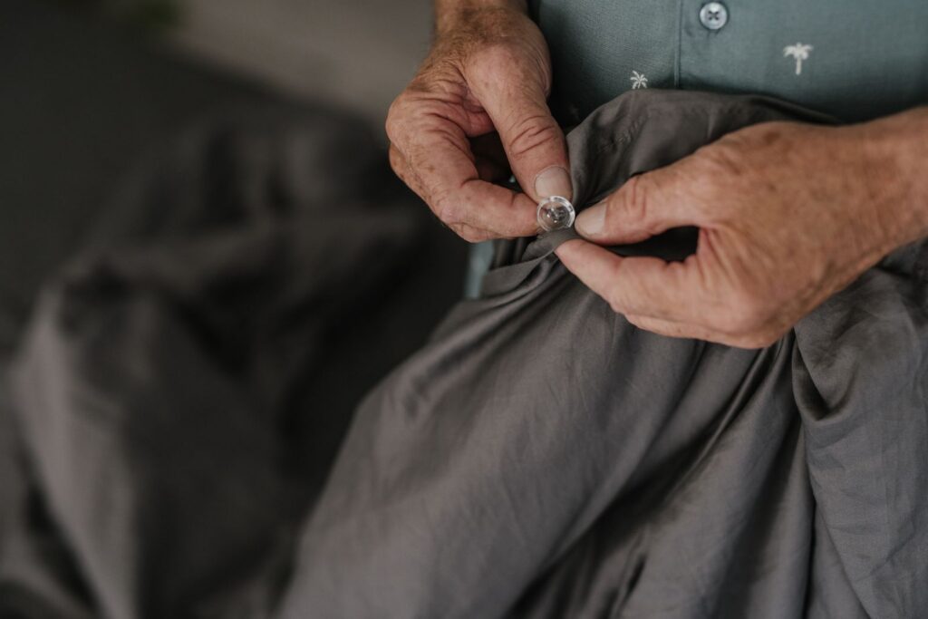 Close-up of senior hands buttoning a grey textile, emphasizing texture and detail.
