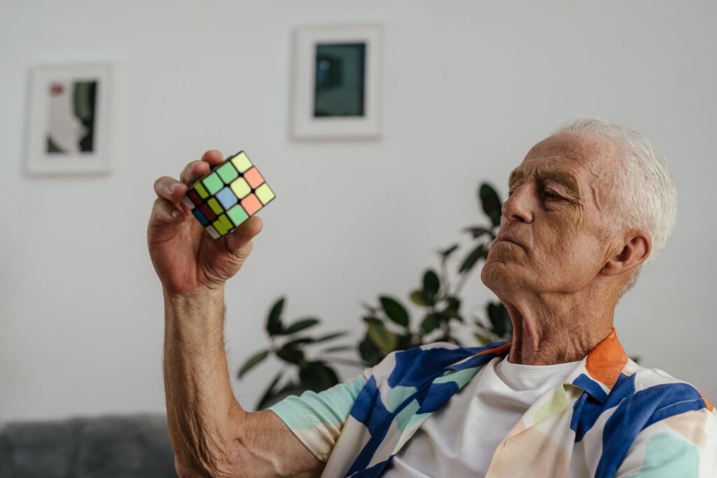 Senior adult contemplating a Rubik's Cube with focus and determination indoors.