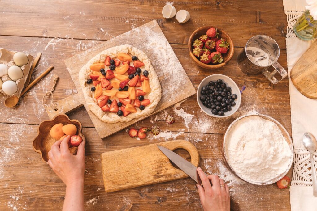 Preparing a homemade fruit tart with fresh berries and peaches on a wooden surface, showcasing baking process.