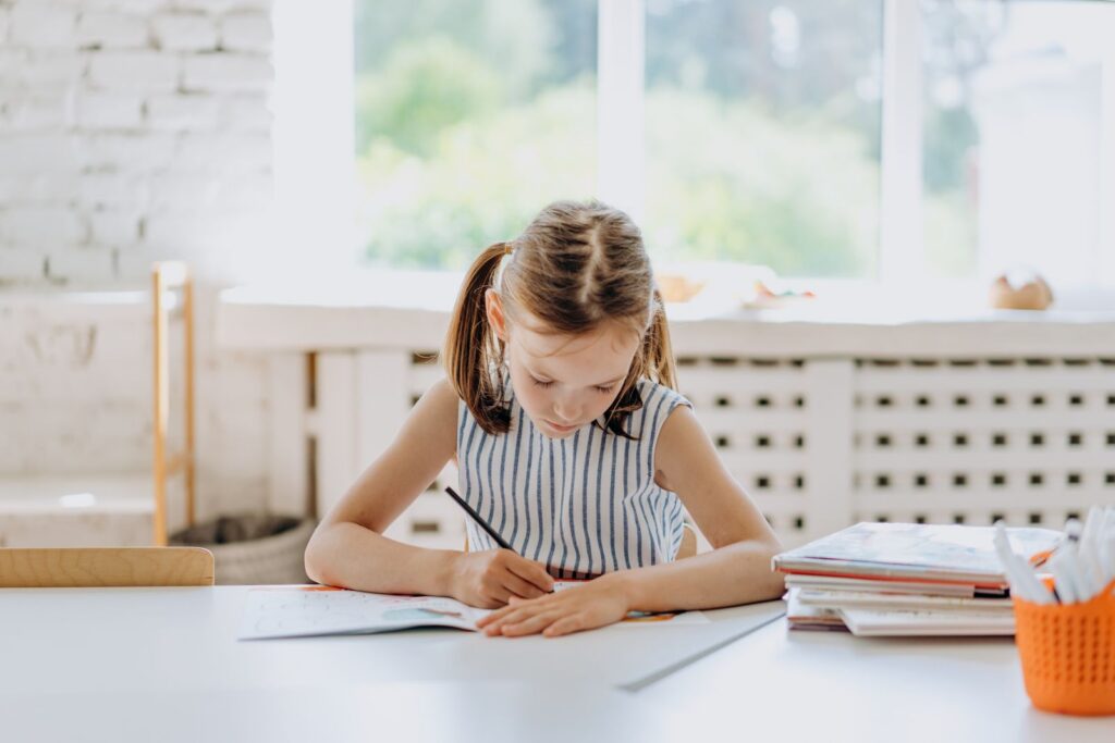 A young girl engaged in coloring at a desk indoors. Bright natural lighting.