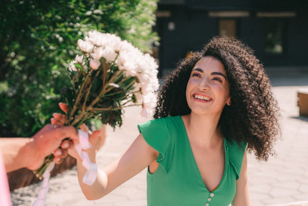 A woman smiles brightly while receiving a bouquet in an outdoor urban setting.