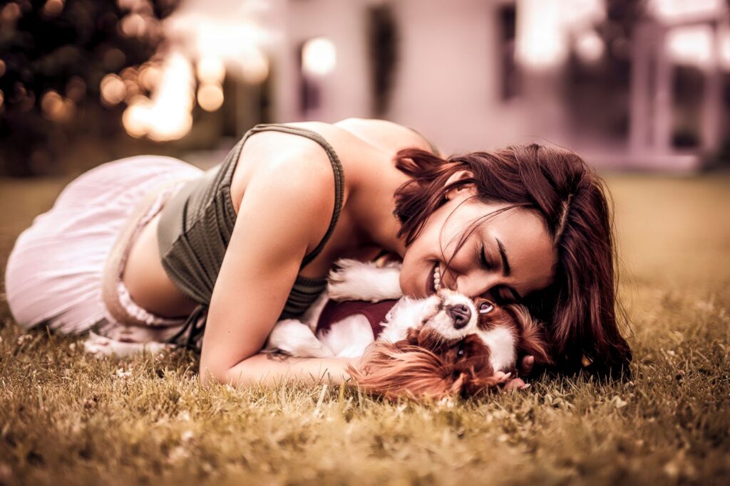 A woman happily cuddling with her Cavalier King Charles Spaniel on the grass.