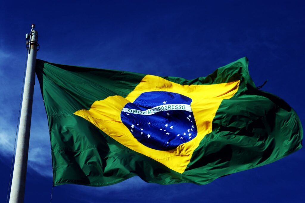 A dynamic shot of the Brazilian flag waving on a flagpole with a clear blue sky background.