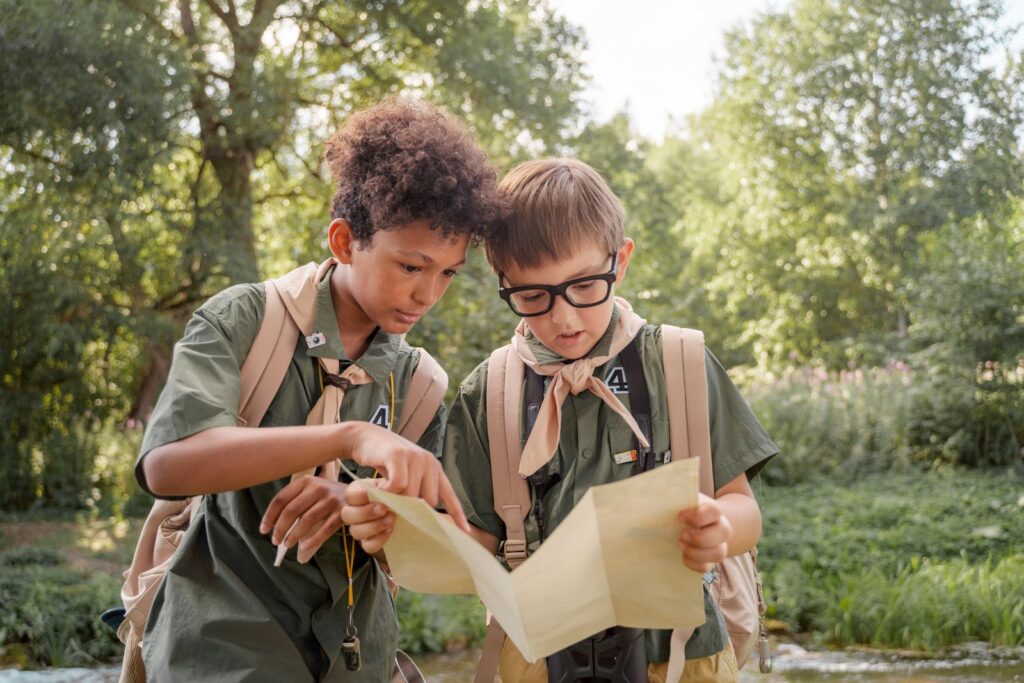 Two boys in scouting gear examine a map during an outdoor adventure.