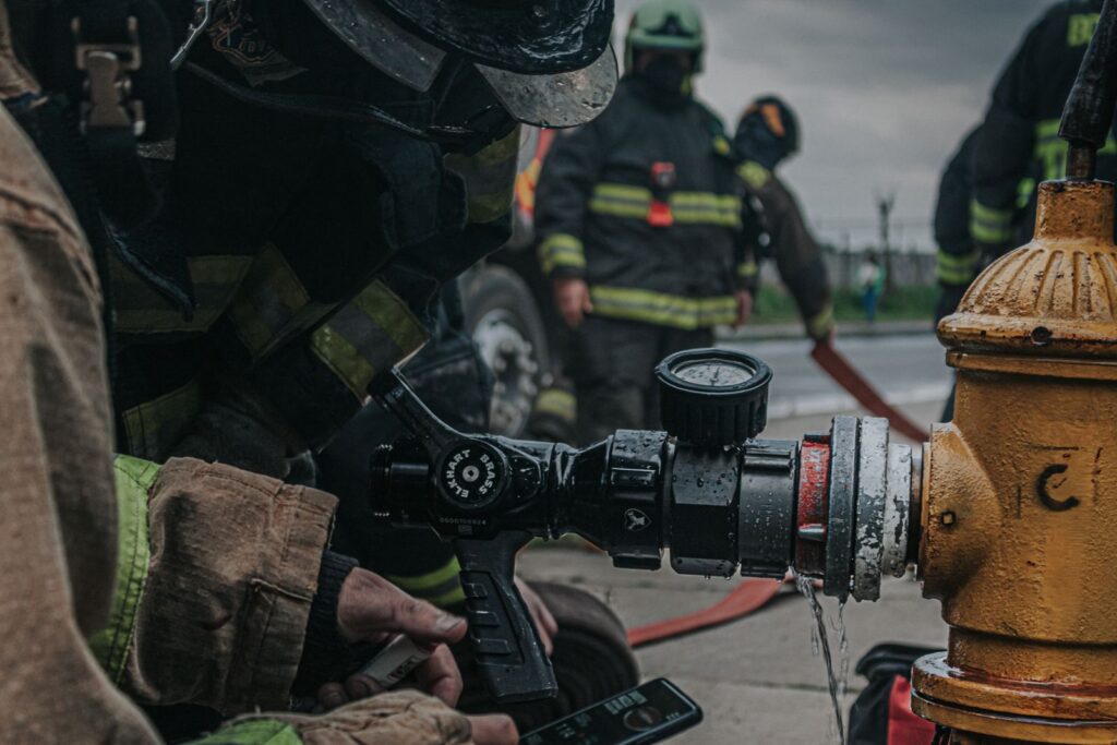 Close-up of firefighters setting a hose by a hydrant, emphasizing teamwork and safety equipment.