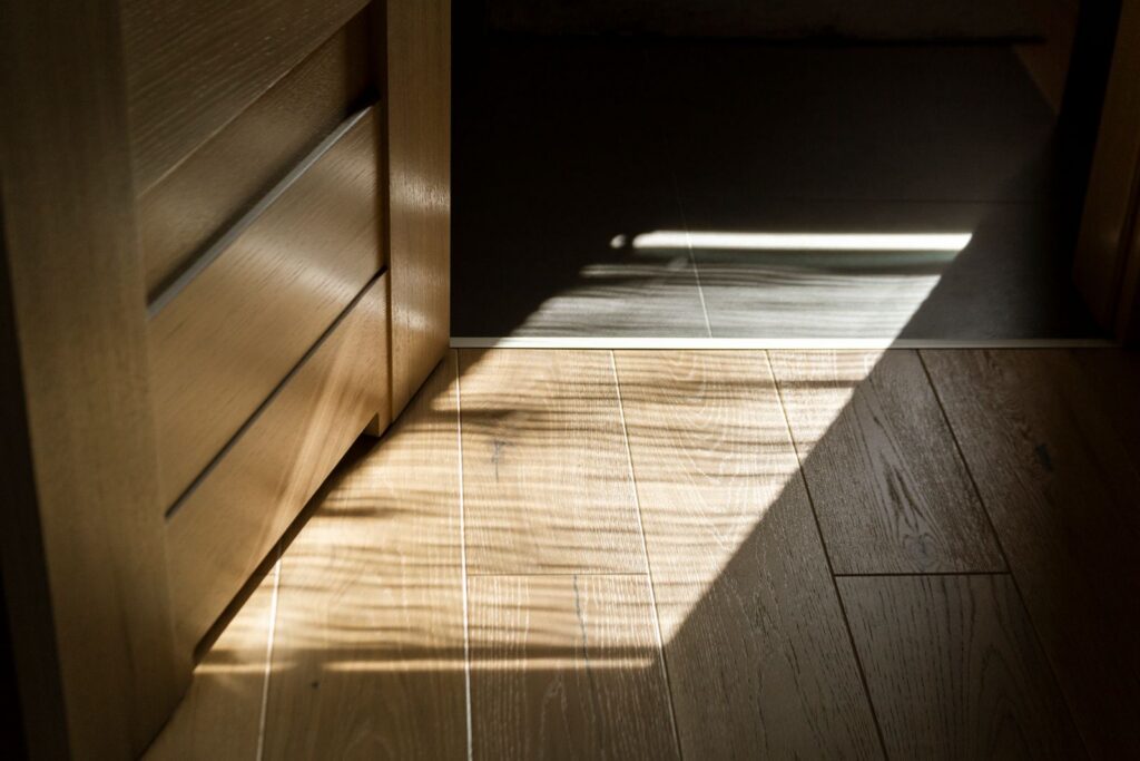 Sunlit shadows create patterns on a wooden parquet floor indoors.