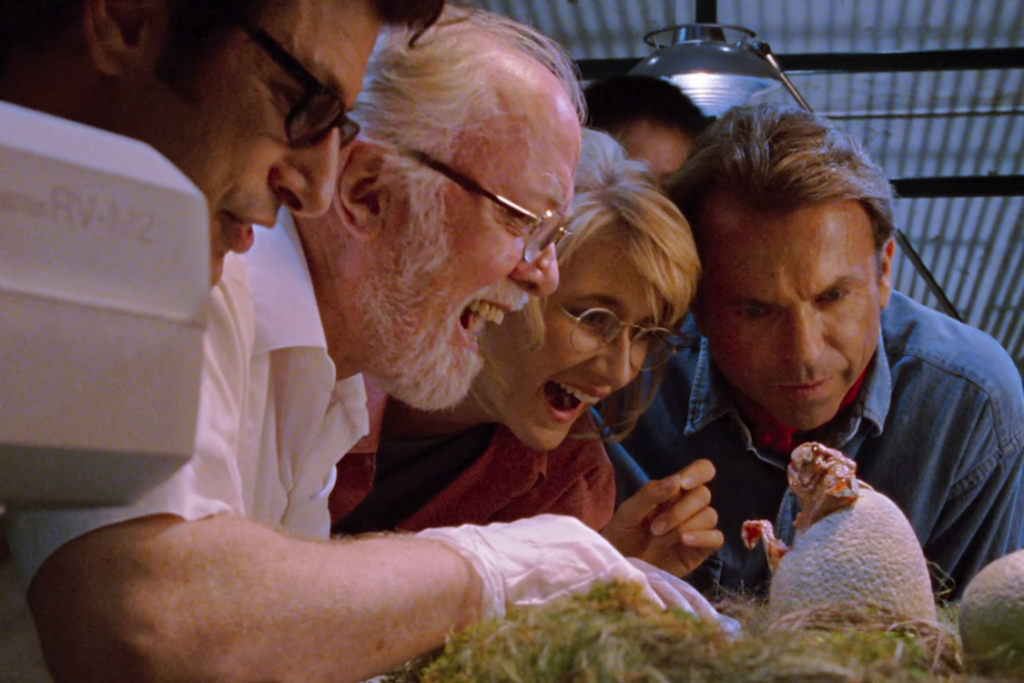 Dr. Alan Grant and the Jurassic Park scientists watch a dinosaur hatch.