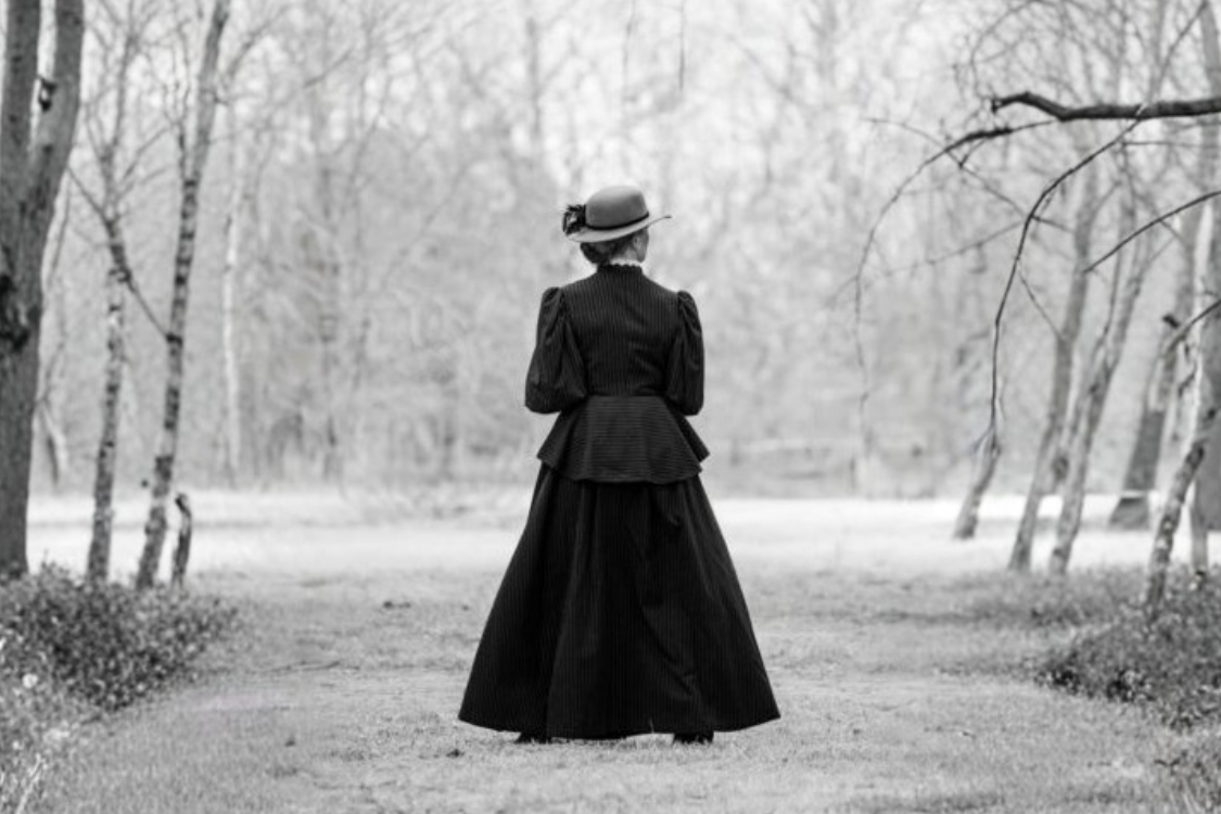 A woman in victorian attire gazes at a landscape.