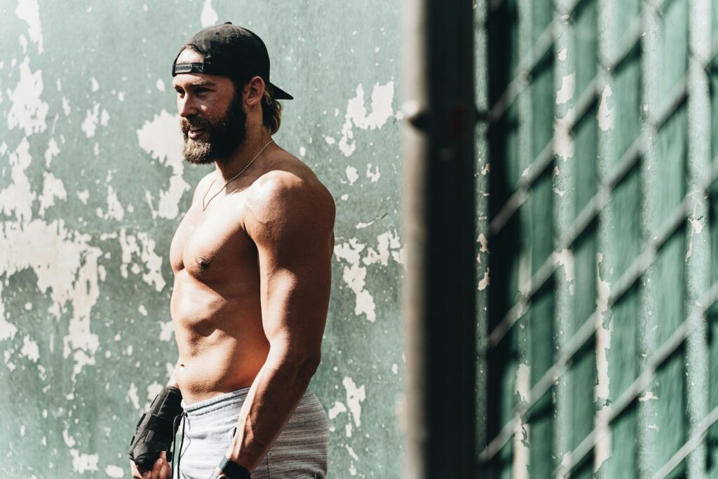 topless man in blue denim jeans standing beside blue wall during daytime