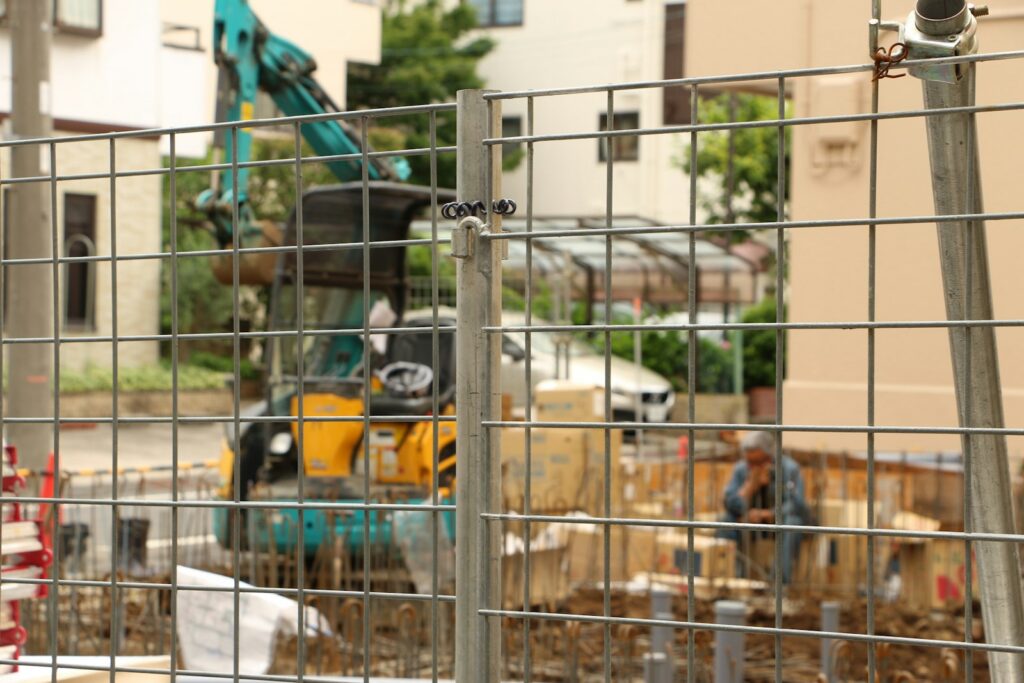 Construction worker operating an excavator behind a fence.