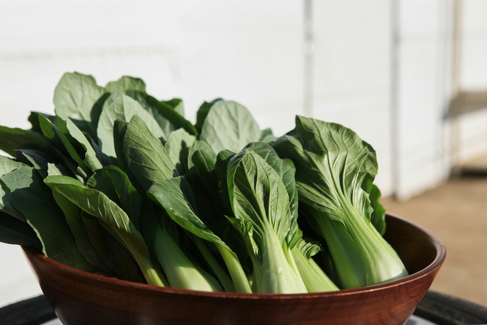 a wooden bowl filled with green bok choy leafy vegetables